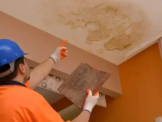 A technician in a hard hat checking a water-stained ceiling panel